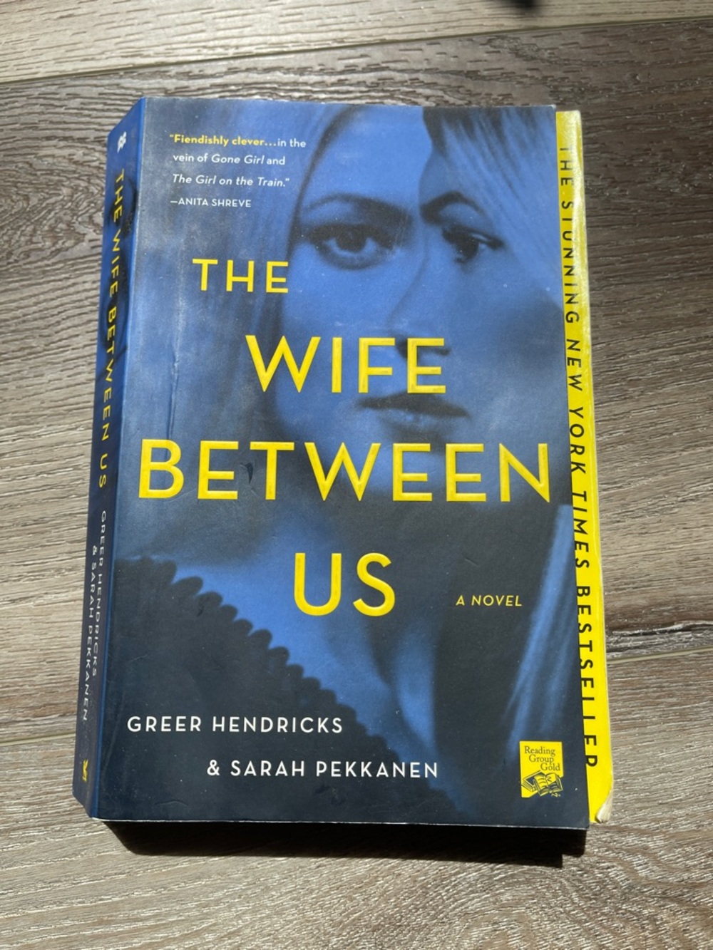 The Wife Between Us - Yellow & Blue Paperback Novel